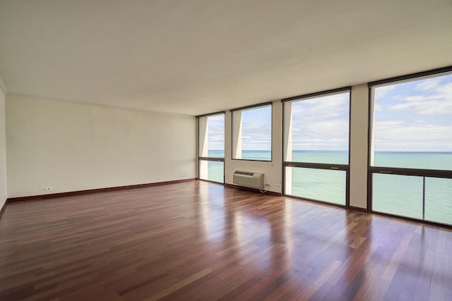 unfurnished room featuring a water view, wood finished floors, a wall mounted air conditioner, and baseboards