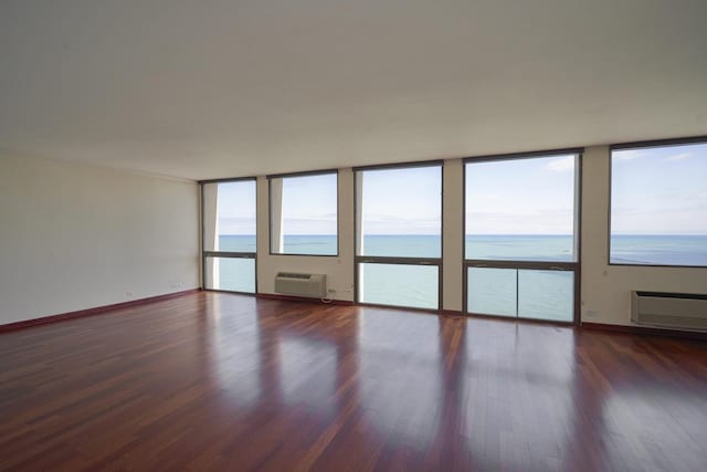 spare room featuring wood finished floors, a wall unit AC, plenty of natural light, a water view, and floor to ceiling windows