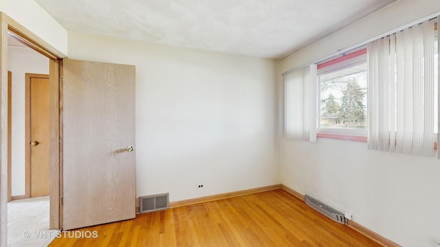 spare room with baseboards, light wood-style flooring, and visible vents