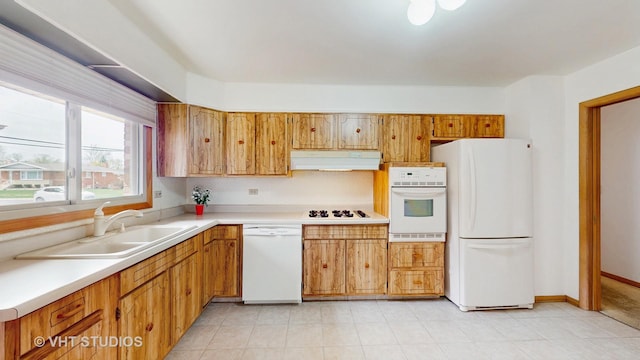 kitchen featuring brown cabinetry, white appliances, light countertops, under cabinet range hood, and a sink