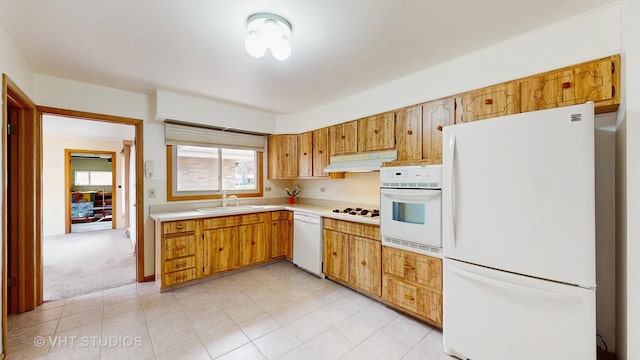 kitchen with white appliances, light countertops, under cabinet range hood, a sink, and light tile patterned floors