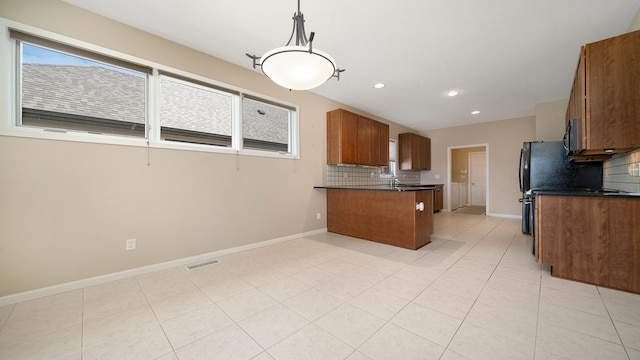 kitchen featuring dark countertops, decorative backsplash, brown cabinetry, and a peninsula