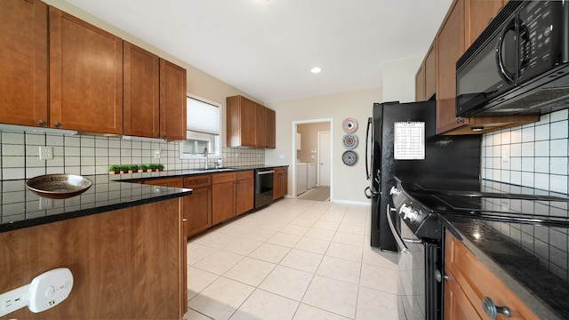 kitchen with decorative backsplash, washing machine and dryer, brown cabinets, a sink, and black appliances