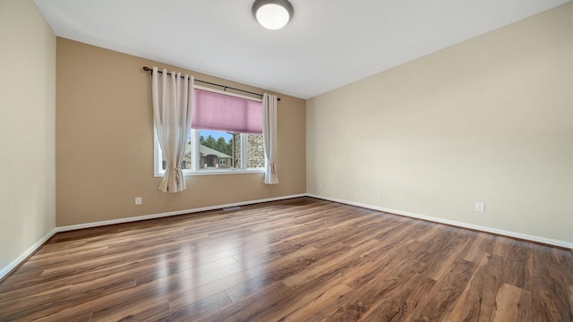empty room featuring baseboards, wood finished floors, and visible vents