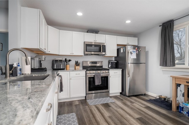 kitchen with white cabinets, dark wood finished floors, light stone counters, stainless steel appliances, and a sink