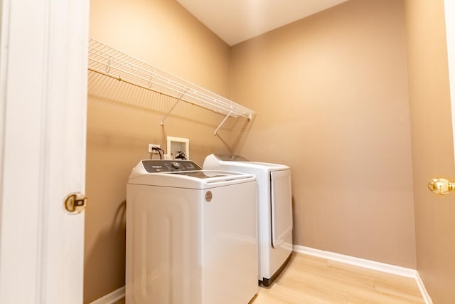 clothes washing area with independent washer and dryer, light wood-type flooring, laundry area, and baseboards