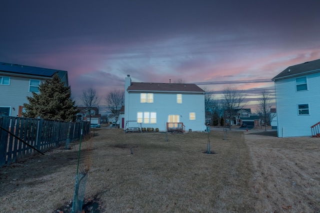 back of house at dusk with a yard and fence