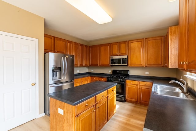 kitchen featuring dark countertops, a kitchen island, stainless steel appliances, light wood finished floors, and a sink
