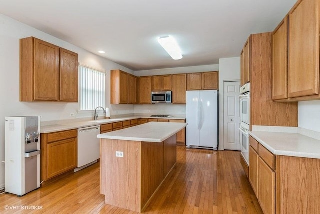 kitchen with light wood-style floors, white appliances, a center island, light countertops, and brown cabinets