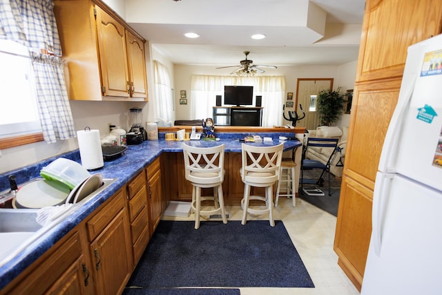 kitchen with freestanding refrigerator, a breakfast bar, a ceiling fan, a peninsula, and recessed lighting