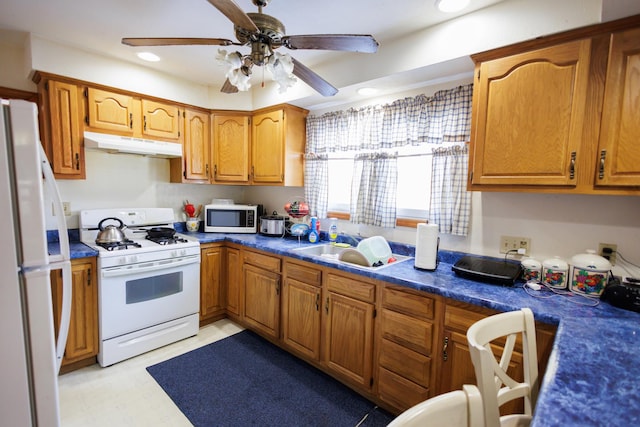 kitchen with white appliances, a ceiling fan, dark countertops, under cabinet range hood, and a sink