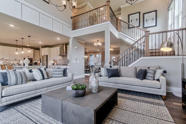 living room featuring dark wood-style flooring, baseboards, a chandelier, a high ceiling, and stairs