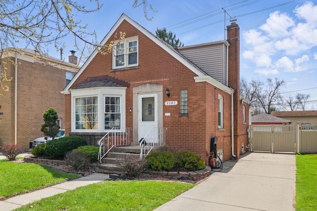 view of front of home featuring a chimney, a gate, fence, brick siding, and a front yard
