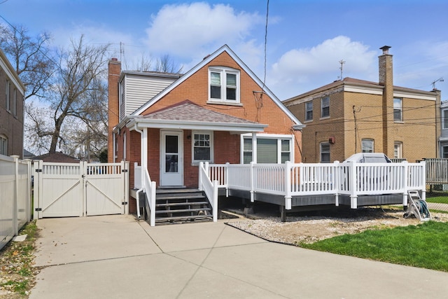 bungalow-style home featuring a chimney, a gate, fence, brick siding, and a deck