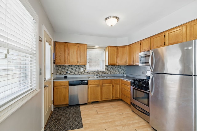kitchen featuring a sink, brown cabinetry, light wood-style floors, stainless steel appliances, and backsplash