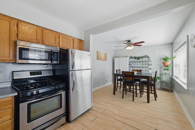 kitchen featuring light wood finished floors, baseboards, ceiling fan, brown cabinetry, and appliances with stainless steel finishes