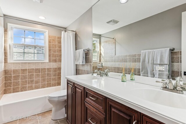 full bath featuring healthy amount of natural light, shower / bath combo with shower curtain, tile patterned flooring, toilet, and tile walls