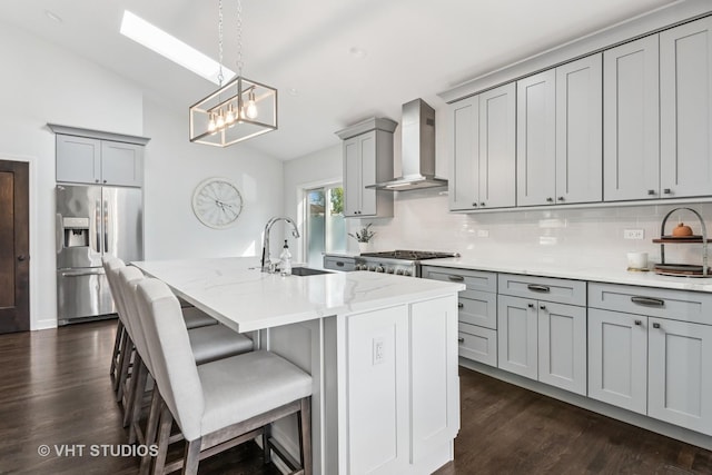 kitchen featuring stainless steel appliances, wall chimney range hood, gray cabinetry, a sink, and tasteful backsplash