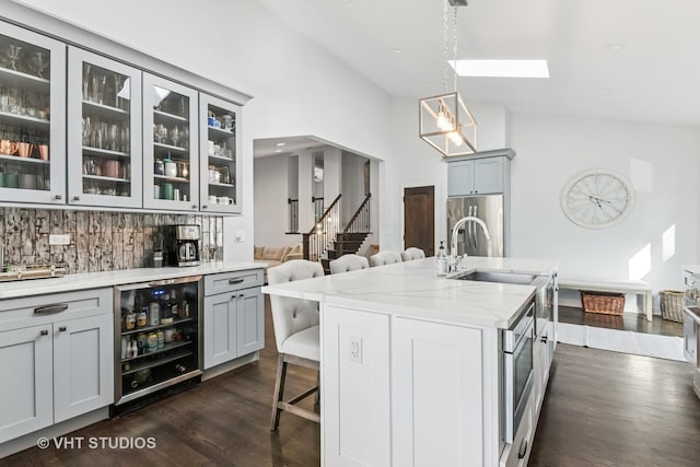 kitchen featuring a breakfast bar, a sink, backsplash, light stone countertops, and dark wood-style flooring