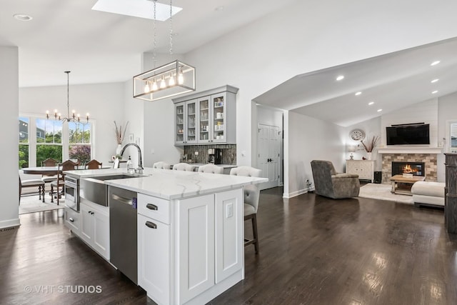 kitchen with stainless steel dishwasher, a sink, a chandelier, a fireplace, and glass insert cabinets