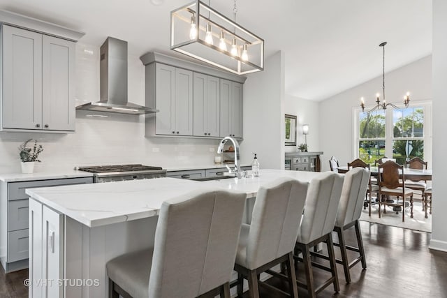 kitchen with gray cabinets, wall chimney range hood, a sink, a chandelier, and vaulted ceiling