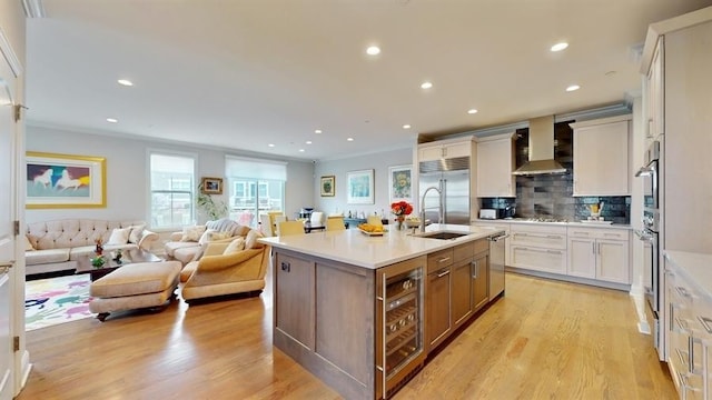 kitchen with wine cooler, a sink, open floor plan, wall chimney range hood, and appliances with stainless steel finishes