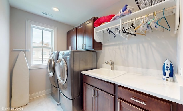 clothes washing area with a sink, cabinet space, visible vents, washing machine and clothes dryer, and baseboards