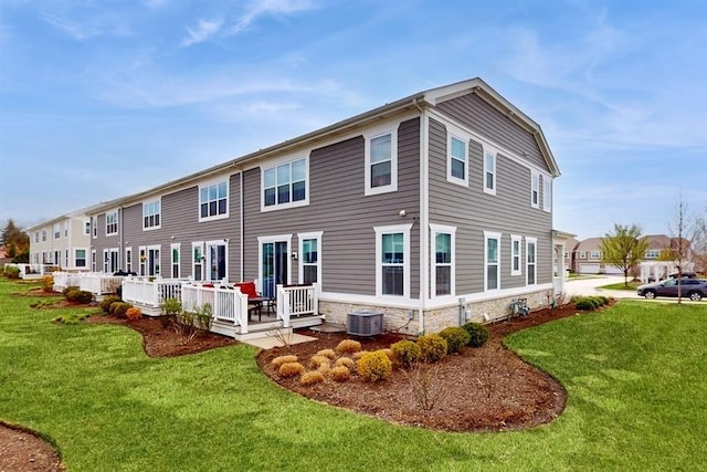 rear view of house with central AC unit, stone siding, a deck, and a lawn
