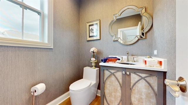 half bathroom featuring vanity, toilet, a wealth of natural light, and wood finished floors
