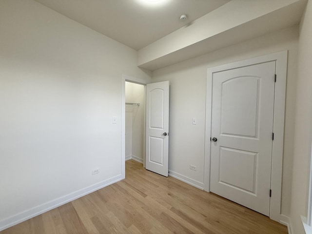 unfurnished bedroom with light wood-style flooring, baseboards, and a spacious closet