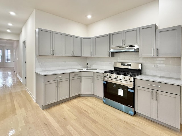 kitchen featuring gray cabinetry, under cabinet range hood, stainless steel gas range oven, and light wood finished floors