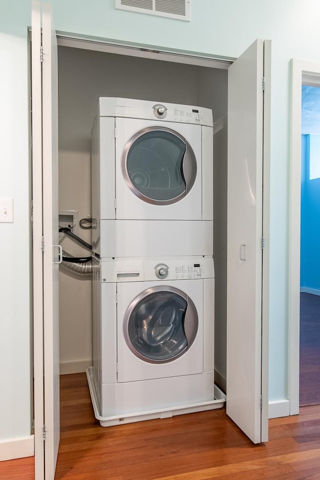 laundry room featuring baseboards, stacked washer and dryer, laundry area, and wood finished floors