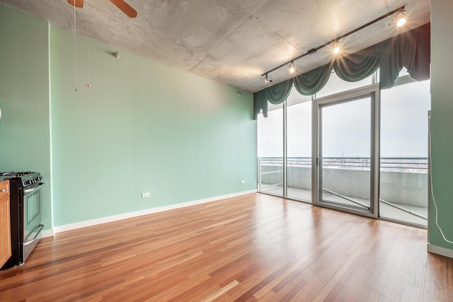 empty room featuring rail lighting, light wood finished floors, baseboards, and a ceiling fan