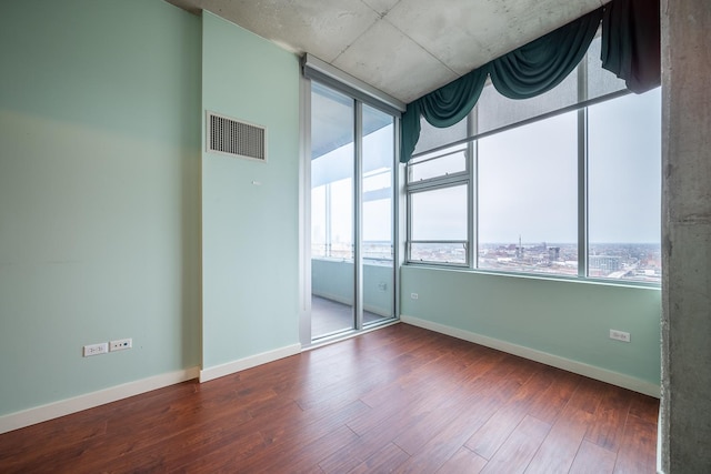 empty room featuring wood finished floors, baseboards, visible vents, and plenty of natural light