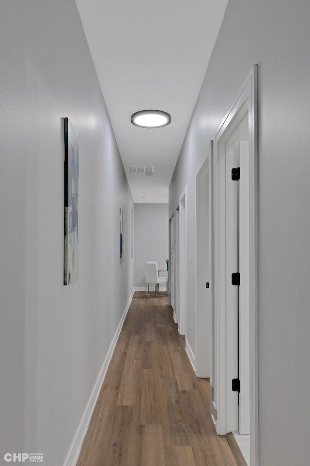 hallway featuring visible vents, baseboards, and wood finished floors