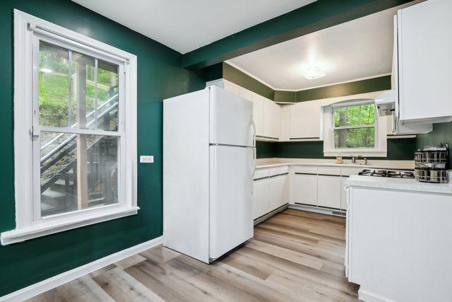 135 Cora Ave, Fox Lake, IL 60020 - kitchen with freestanding refrigerator, white cabinetry, light wood-type flooring, light countertops, and baseboards