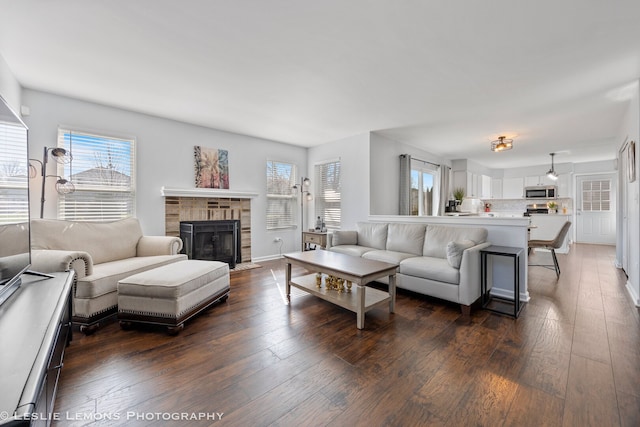 living area with a fireplace with flush hearth, a healthy amount of sunlight, baseboards, and dark wood-style flooring