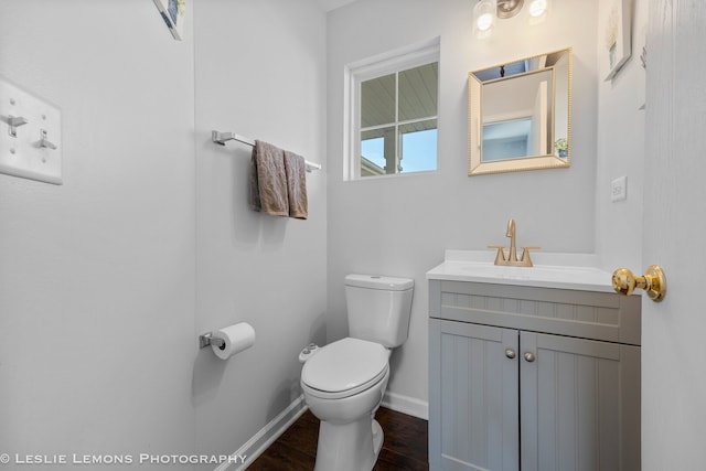 half bath with toilet, vanity, wood finished floors, and baseboards