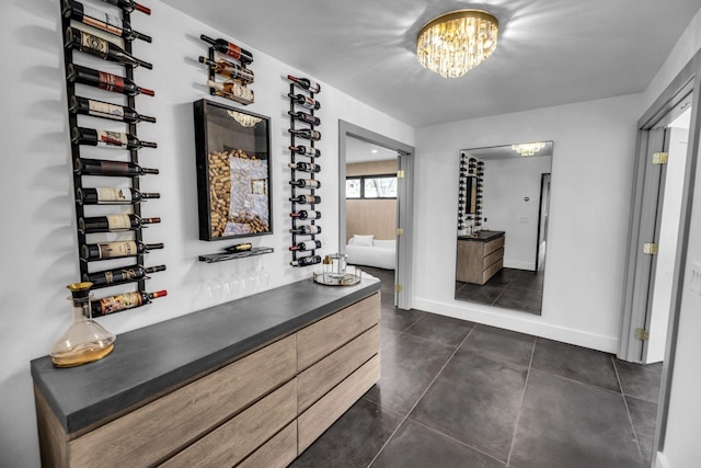 interior space with dark tile patterned flooring, a bar, baseboards, and a notable chandelier