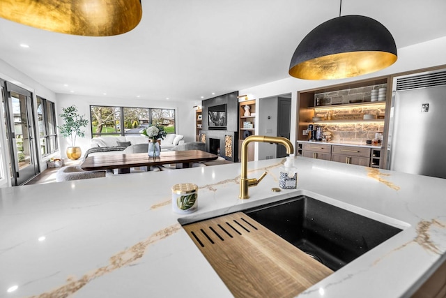 kitchen with light stone counters, a sink, a fireplace, decorative light fixtures, and recessed lighting