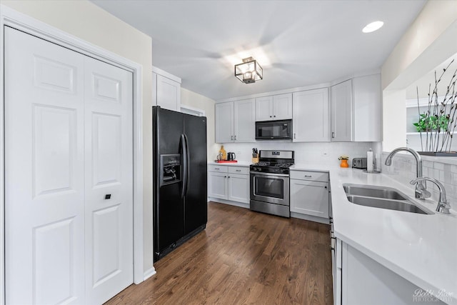 kitchen with a sink, black appliances, light countertops, backsplash, and dark wood-style floors