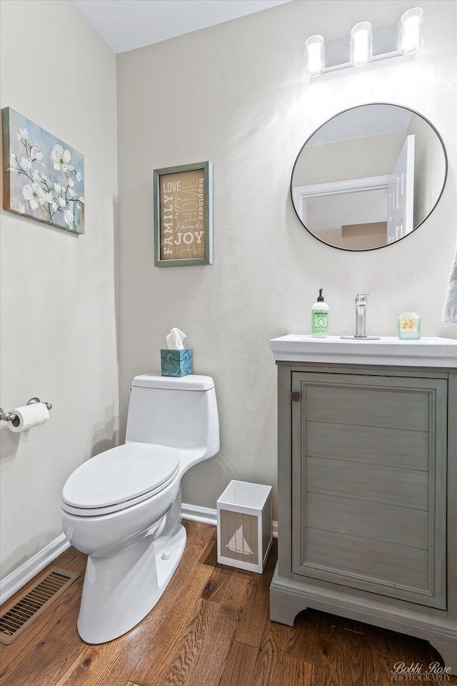half bath featuring wood finished floors, vanity, baseboards, toilet, and visible vents