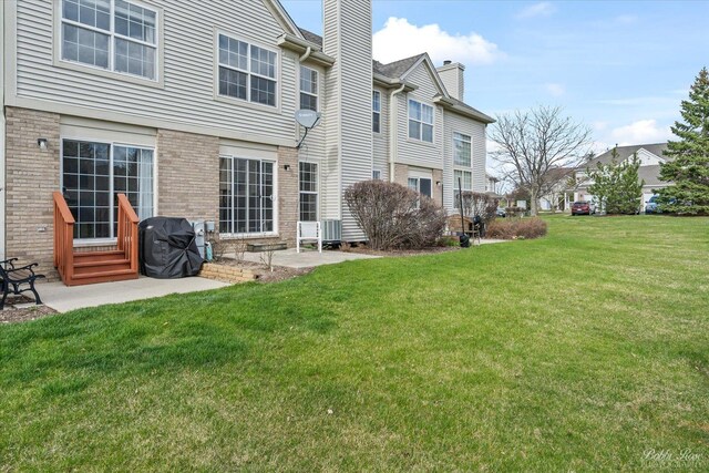 rear view of property with a chimney, brick siding, a patio area, entry steps, and a lawn