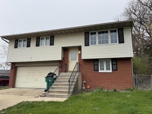 raised ranch with a front lawn, driveway, fence, brick siding, and a garage