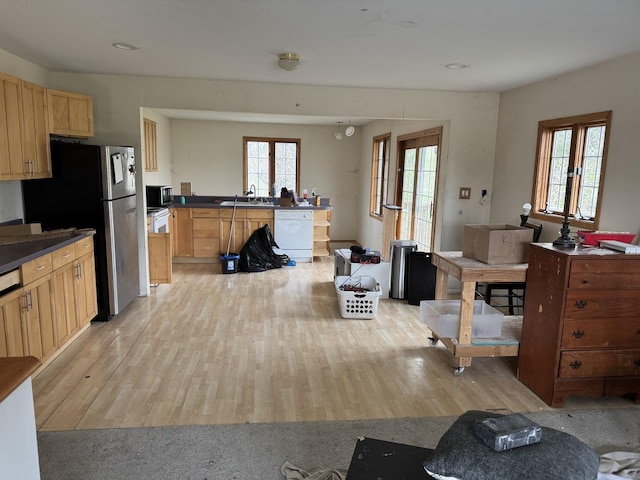 kitchen featuring dark countertops, dishwasher, a sink, and light wood-style flooring
