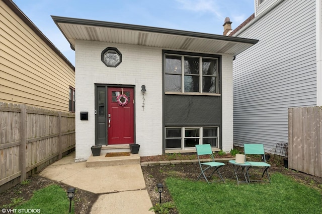 doorway to property with brick siding and fence