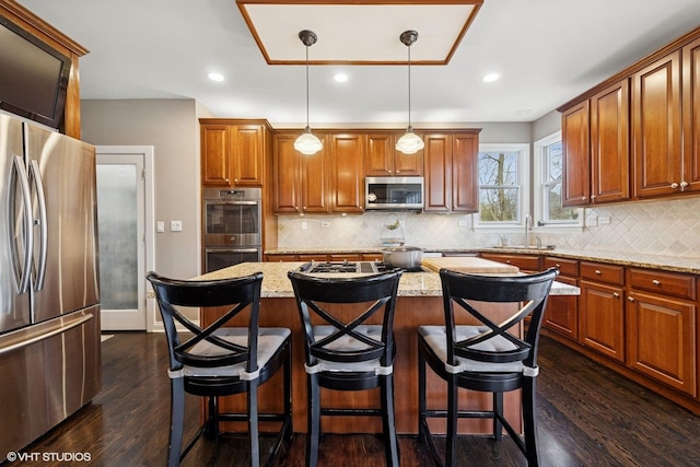 kitchen with dark wood-style flooring, stainless steel appliances, brown cabinetry, and a sink