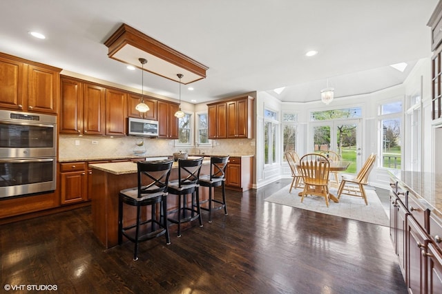 kitchen with light stone countertops, dark wood-style flooring, a breakfast bar, and stainless steel appliances