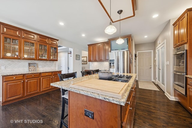 kitchen with a breakfast bar area, dark wood-type flooring, brown cabinets, tasteful backsplash, and stainless steel appliances