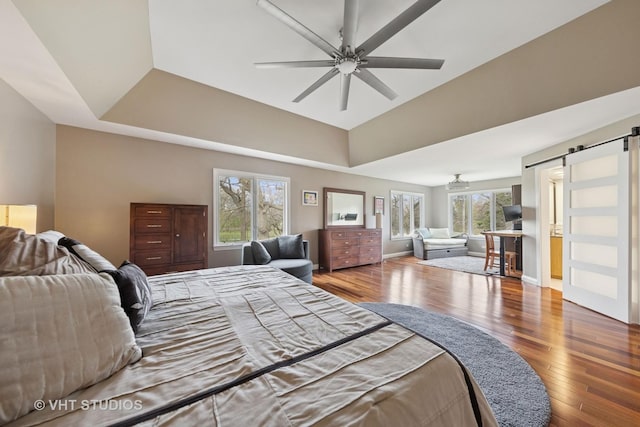 bedroom featuring a tray ceiling, a barn door, wood finished floors, and lofted ceiling